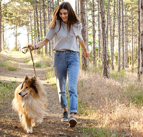 A woman walking her dog in a forest 