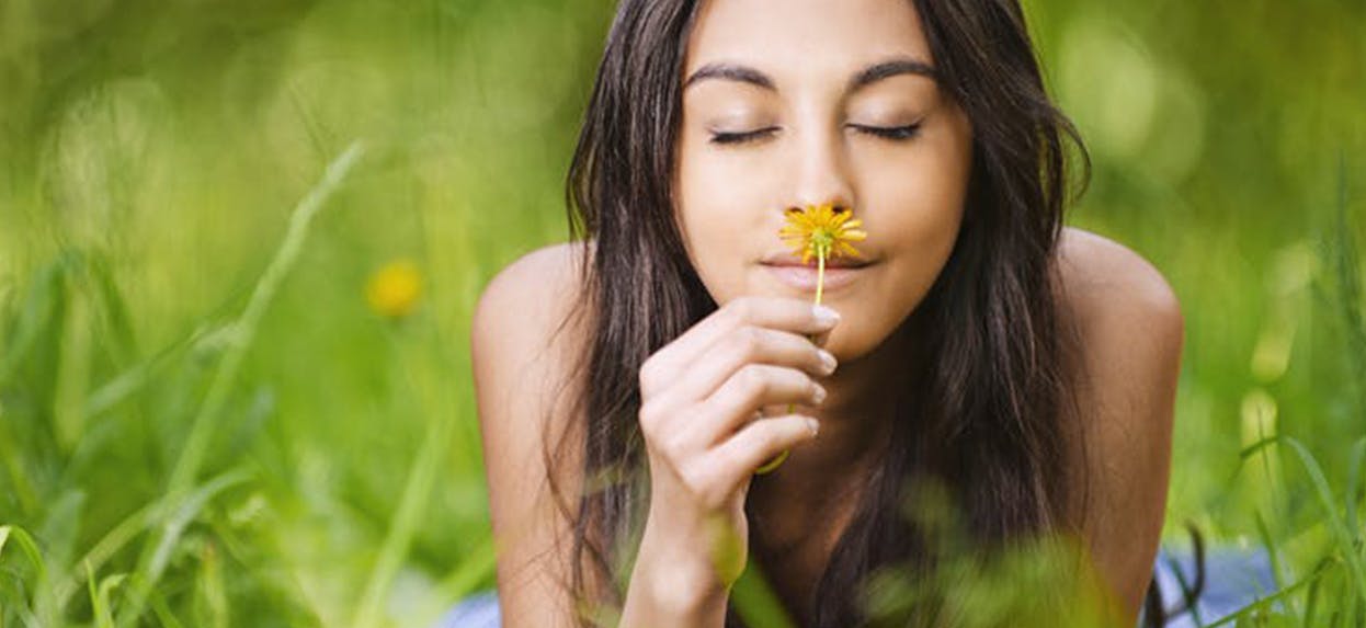 Une femme étendue dans l’herbe haute sent une fleur