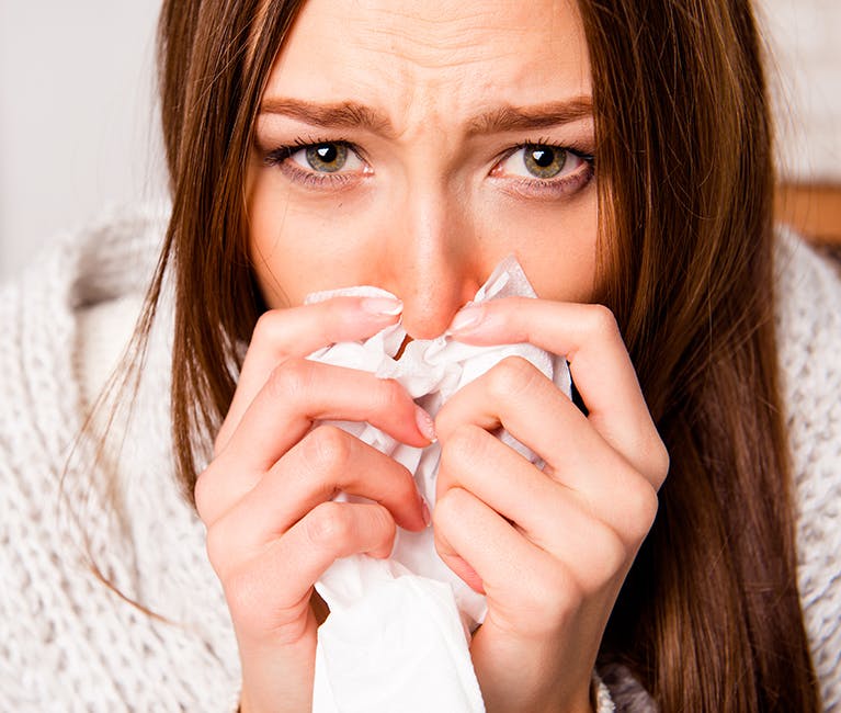 364438334 Woman at home on sofa wrapped in blanket blowing her nose