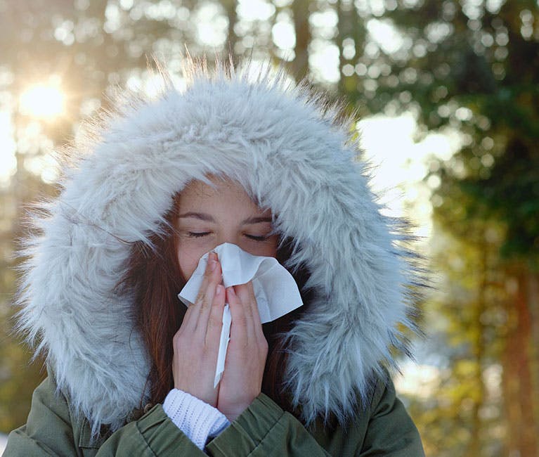 Woman is blowing her congested nose in the cold winter air.