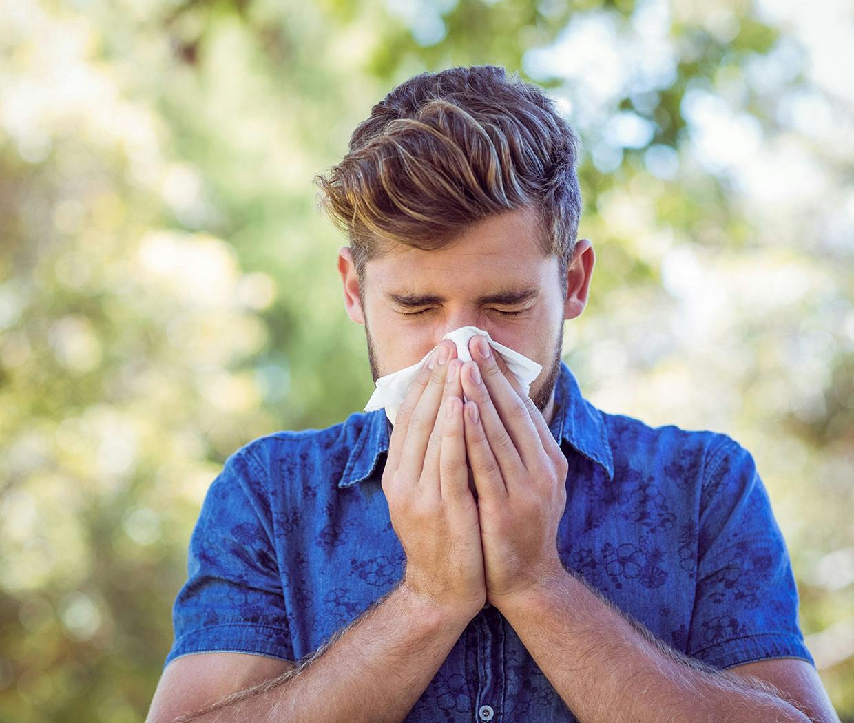 Ein junger Mann hat Heuschnupfen Symptome und niest in ein Taschentuch.