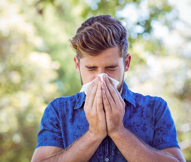 Ein junger Mann hat Heuschnupfen Symptome und niest in ein Taschentuch.