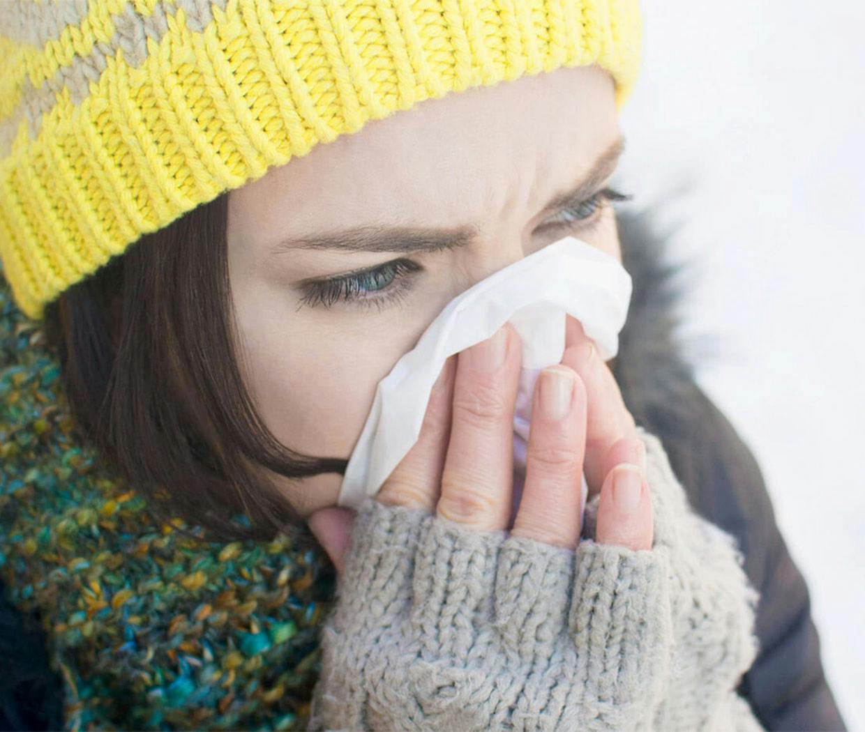 Woman dressed in winter clothing blowing her nose
