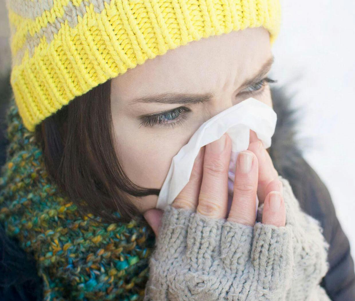 Woman dressed in winter clothing blowing her nose