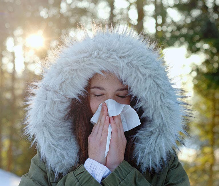 Woman is blowing her congested nose in the cold winter air.