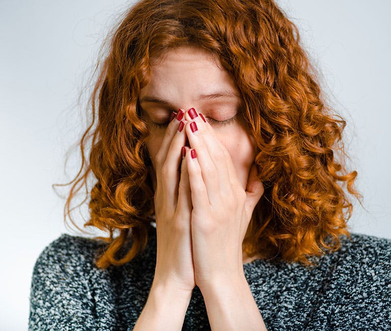 A long-haired woman has both hands over her nose and mouth and tries to cough