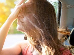 Passenger in car lifts face to open window and smoothes hair from her face