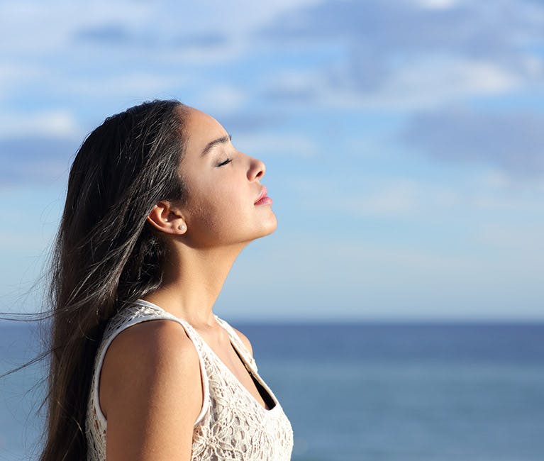 Woman wearing a hat and scarf with head tilted up breathing in the fresh air