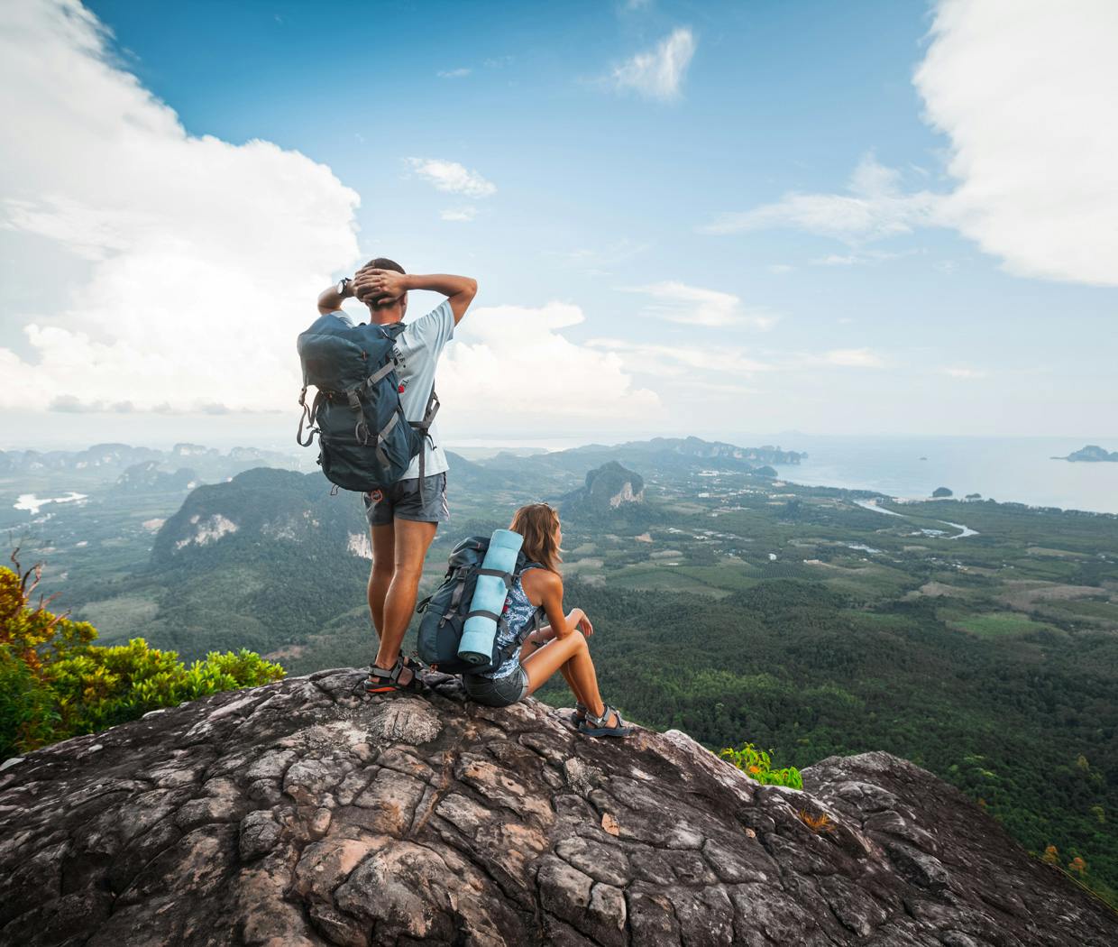 Man and woman stand on top of rock cliff as they gaze into the horizon 