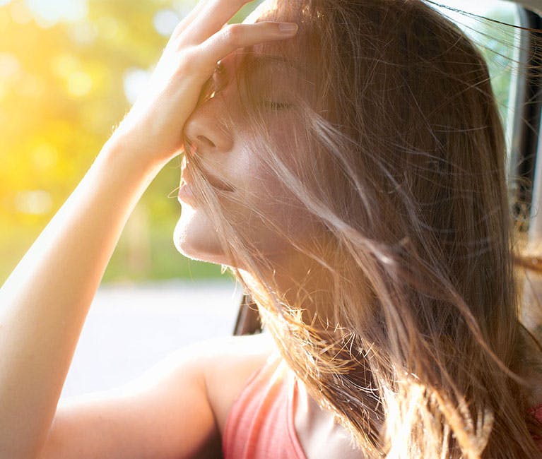 Passenger in car lifts face to open window and smoothes hair from face