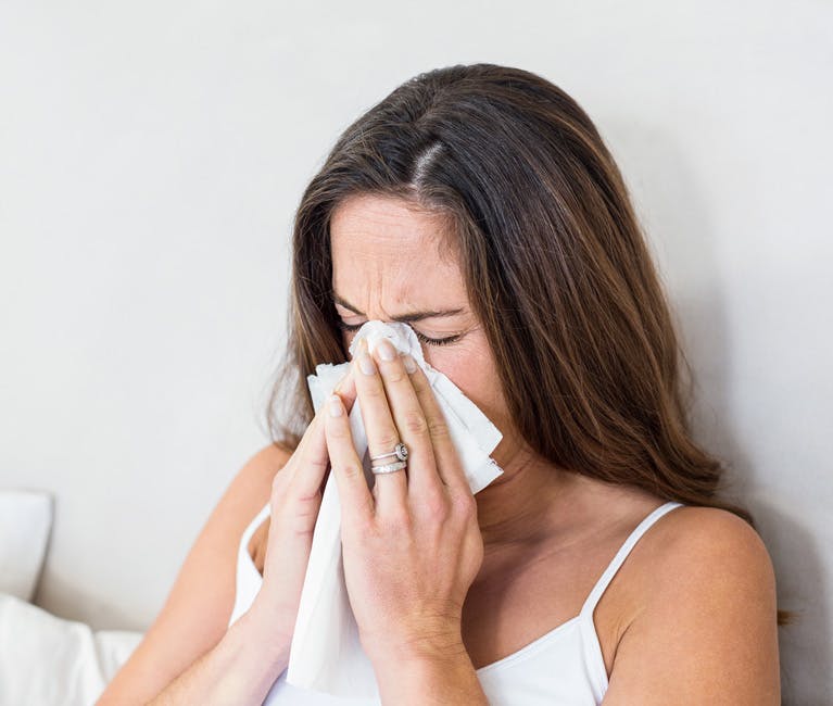 Woman dressed in white singlet blowing her nose with a tissue