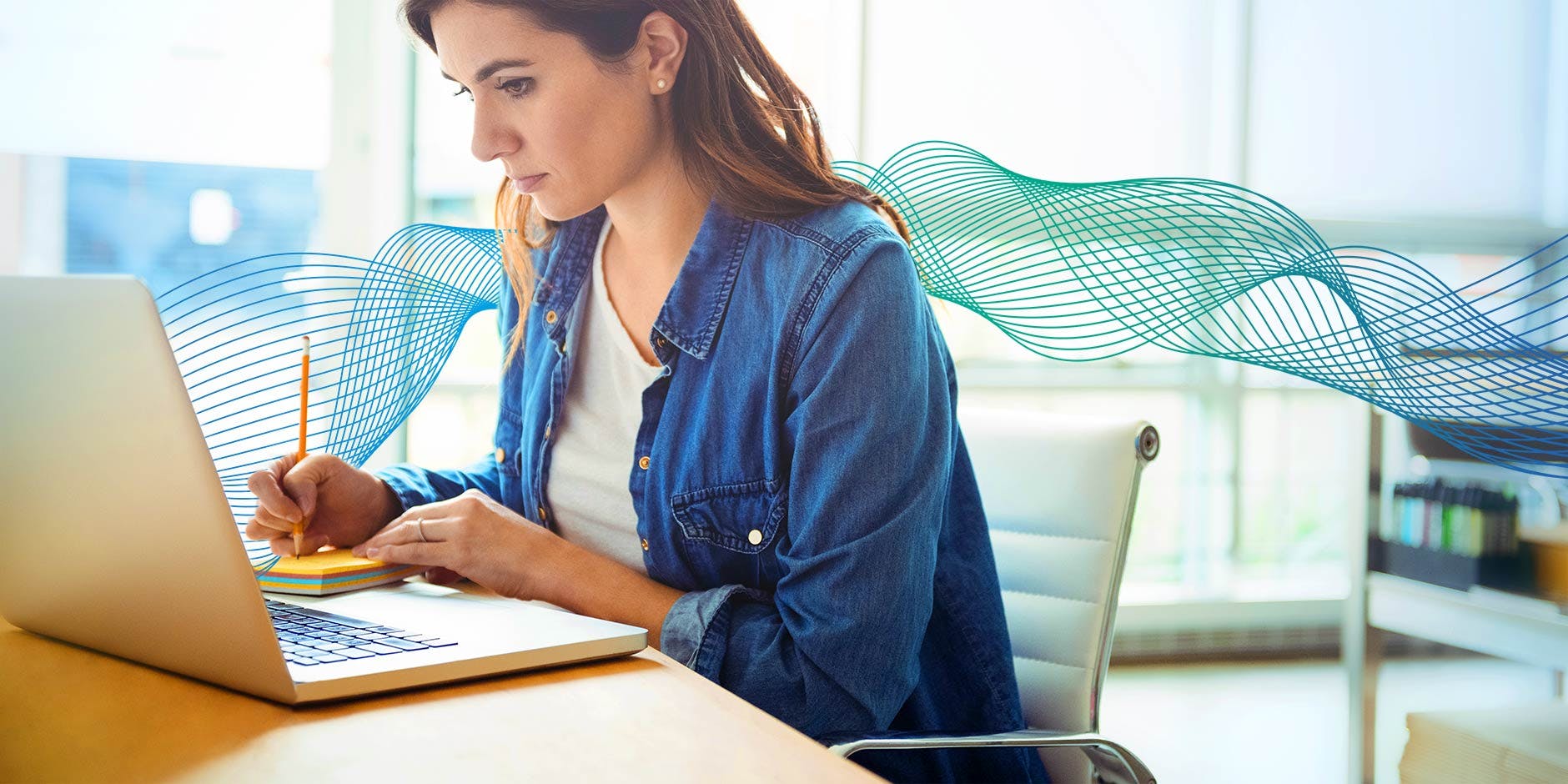 Cadre d'un environnement de bureau avec une femme prenant des notes assise à un ordinateur portable 