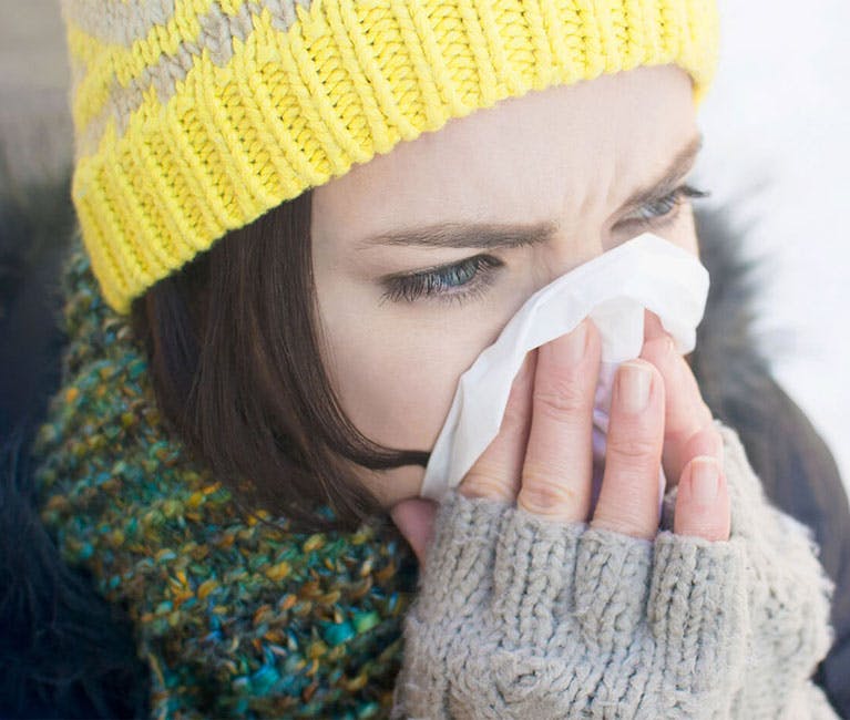 Woman dressed in winter clothing blowing her nose