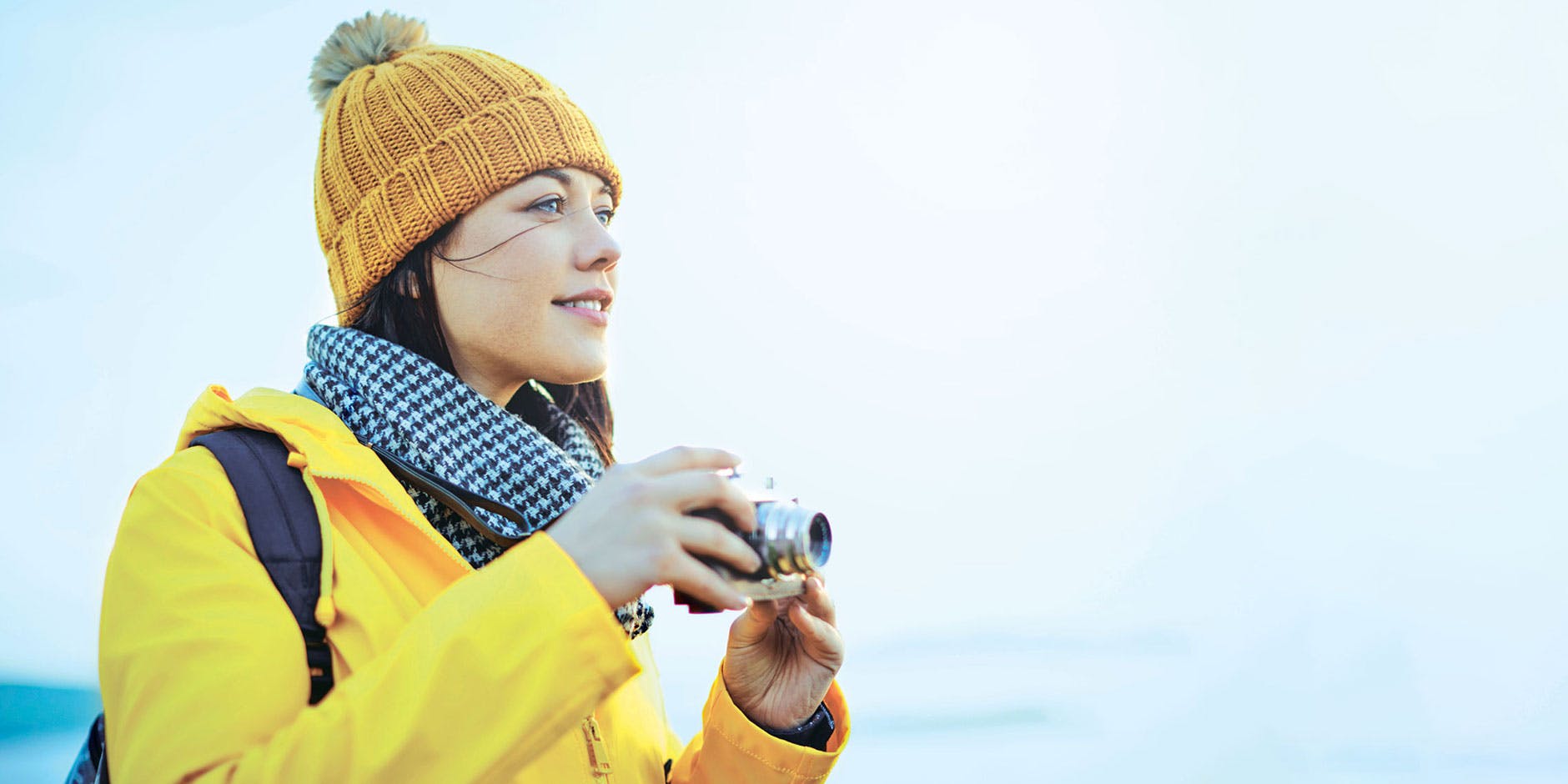 Kvinne med hatt, jakke og skjerf tar bilder av landskapet. 