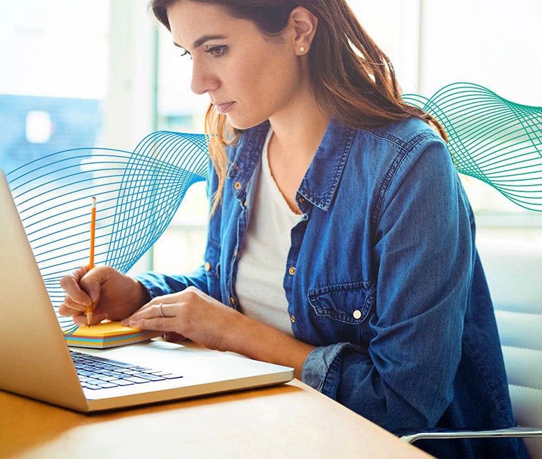 Set in an office environment with woman sitting at laptop writing notes