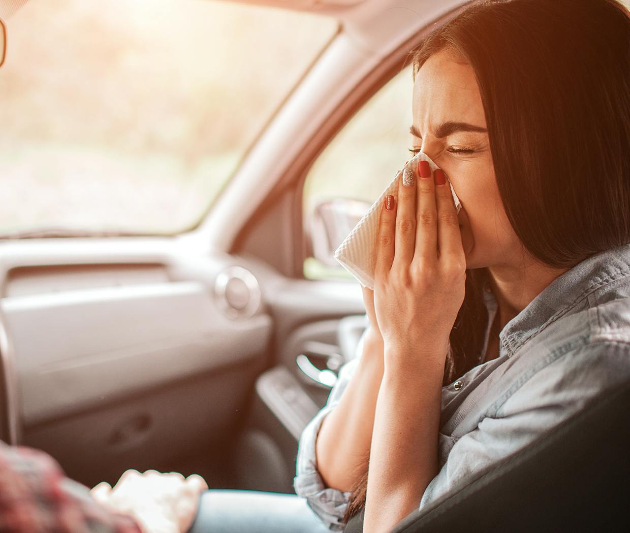 Femeie aflată în mașină și care își suflă nasul