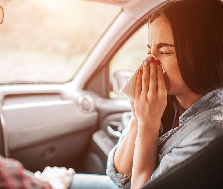 Femeie aflată în mașină și care își suflă nasul