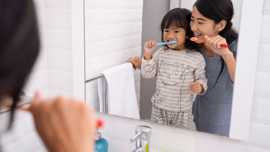 Mother helping young daughter brush teeth