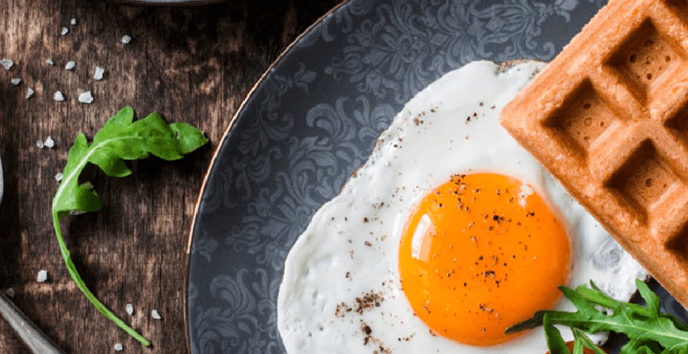 Sunny side up eggs, Belgian waffle, and arugula salad on a plate