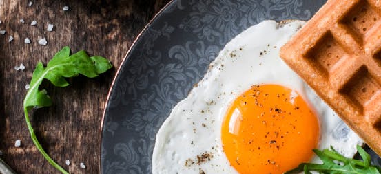 Sunny side up eggs, Belgian waffle, and arugula salad on a plate