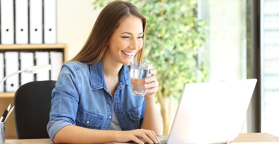 Woman drinking water and looking at her laptop Woman drinking water and looking at her laptop