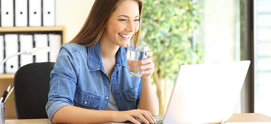 Woman drinking water and looking at her laptop Woman drinking water and looking at her laptop