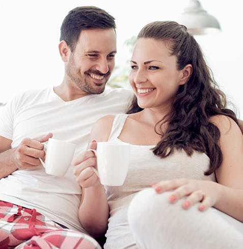 Happy couple in pajamas relaxes on couch with warm drinks in the morning
