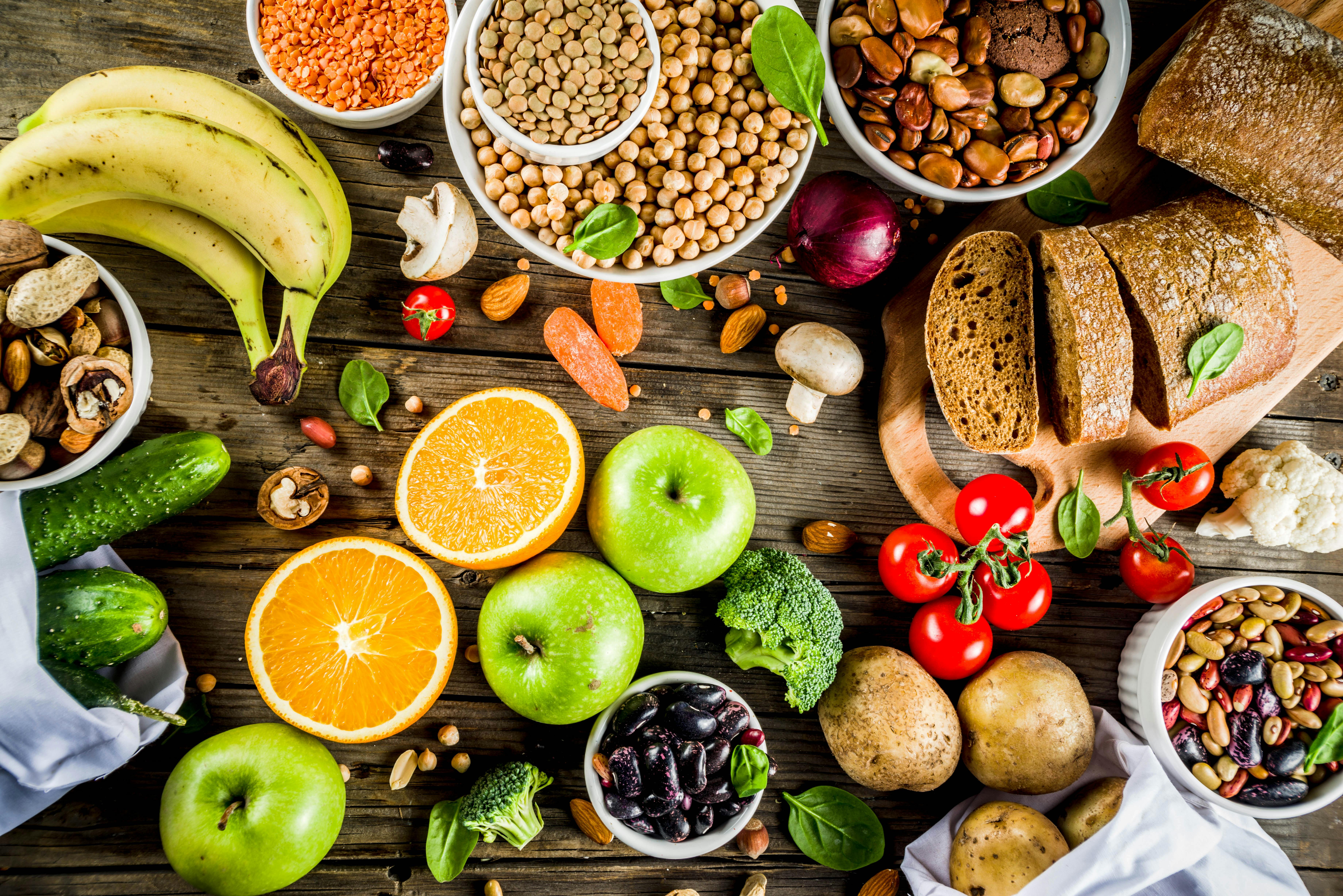 Fruits, veggies, whole grain bread, nuts, beans, and potatoes on a wooden table