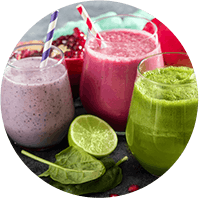 Three different smoothies – in purple, red, and green – side by side, with fruits and vegetables next to them 