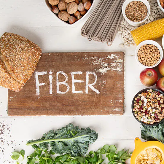 Foods high in fiber on a white background, including bread, chia seeds, nuts, beans, broccoli, apples, and greens.