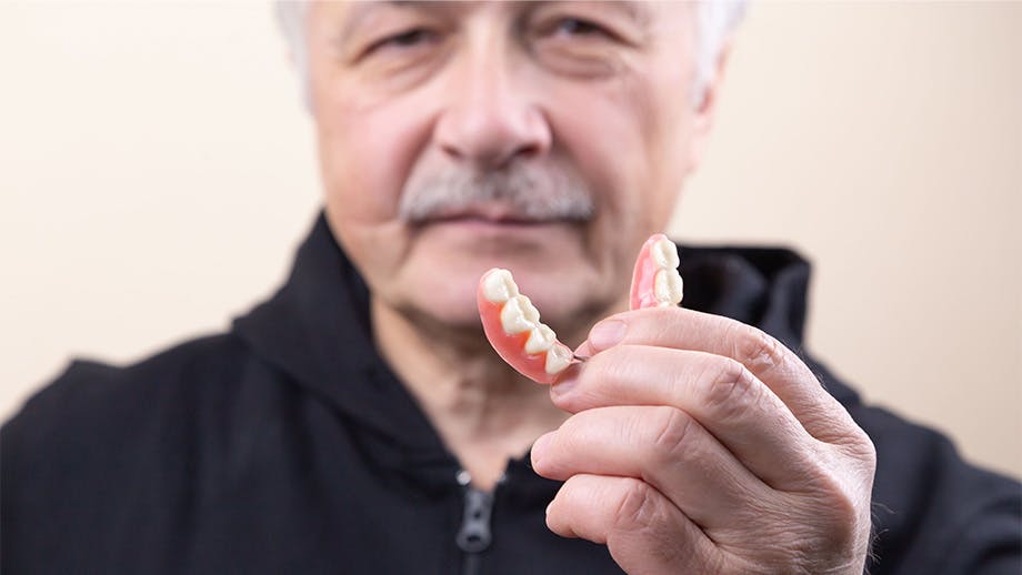 Older man with gray hair holds a partial denture