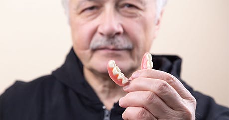 Older man with gray hair holds a partial denture