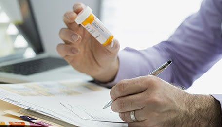 Doctor holding a pill bottle and writing a prescription