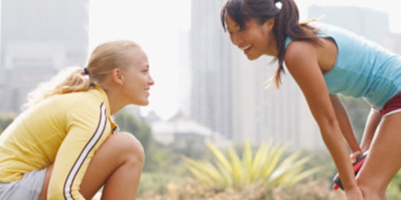 Two young woman doing stretching in the park, smiling