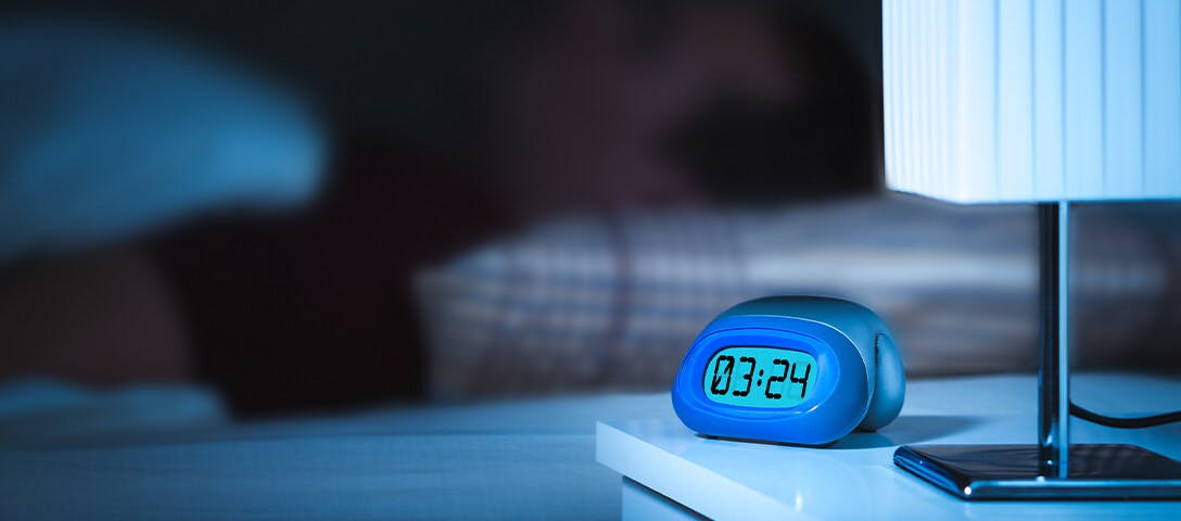 Man sleeping in bed with a digital clock showing 3:24am