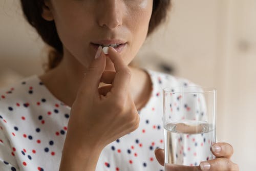 Close up cropped shot of young lady holding a glass of water preparing to swallow a pill