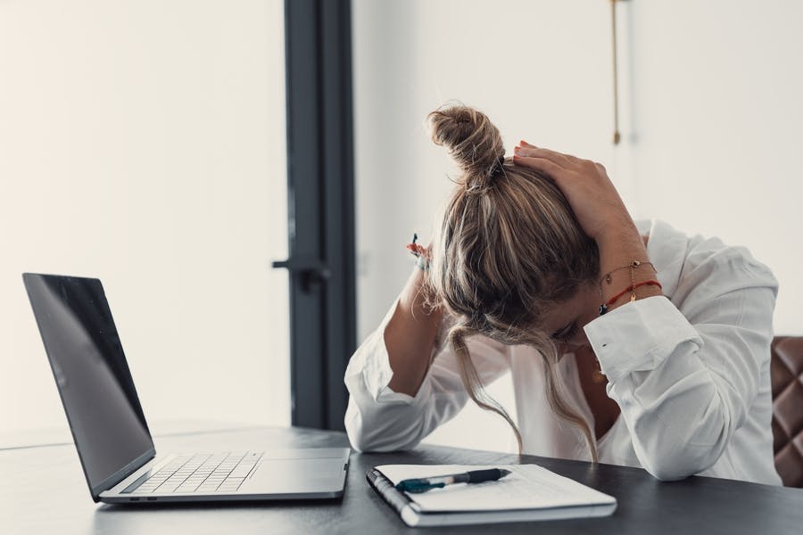 Woman at work at a computer is suffering from a headache and has her head in her hands