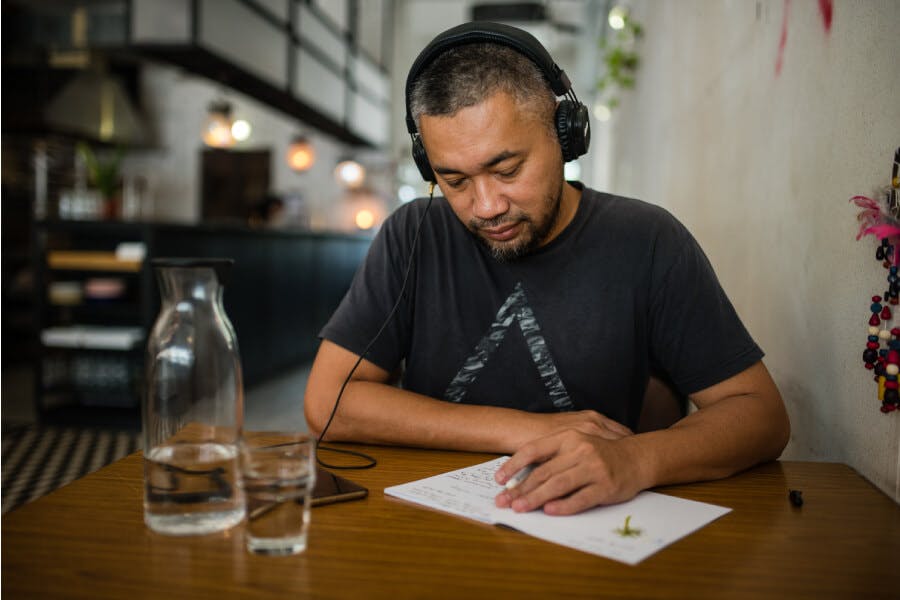 Man in cafe listening to something on headphones and taking notes