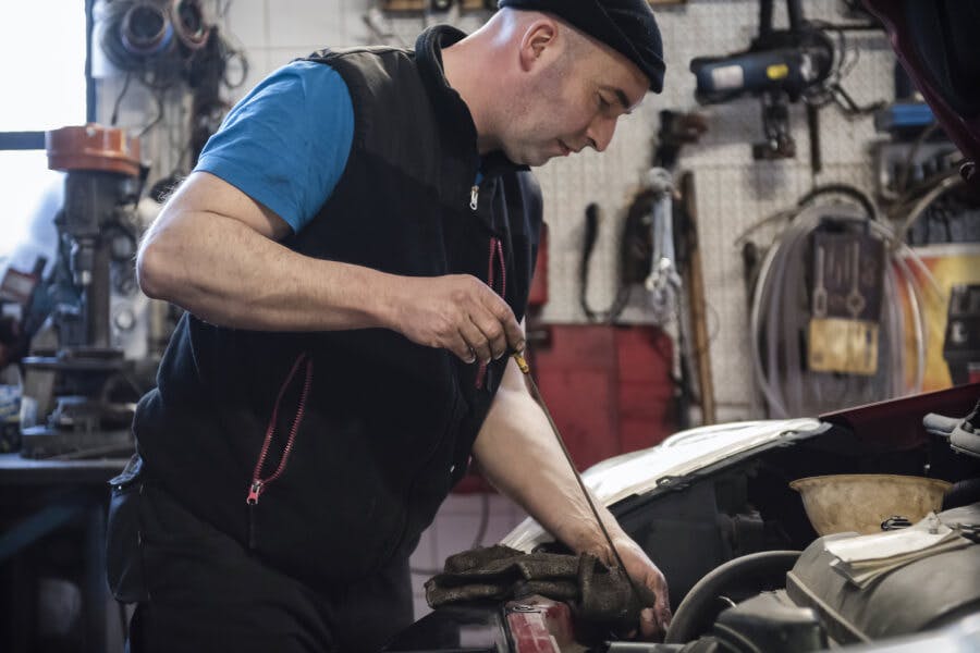 Male mechanic checking oil under the hood of a car Male mechanic checking oil under the hood of a car