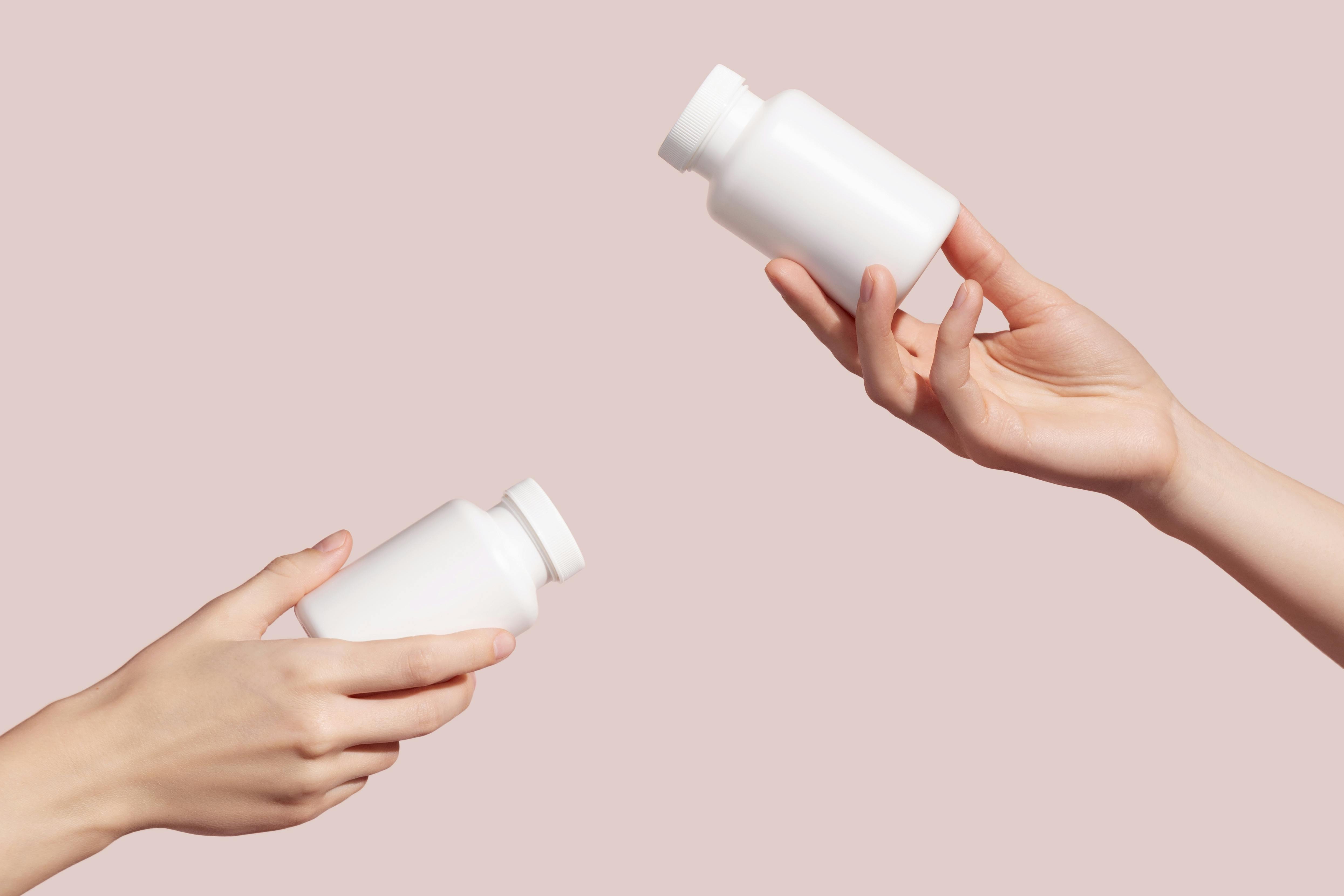 Two hands holding plain white pill bottles 