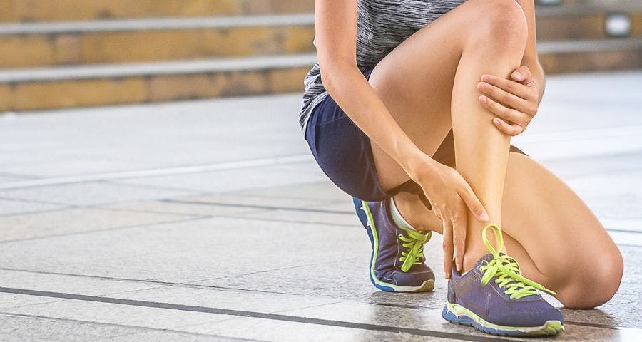 Injured female runner kneeling down to clutch her right ankle
