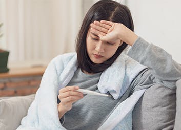 Young woman with hand on her forehead reading a thermometer