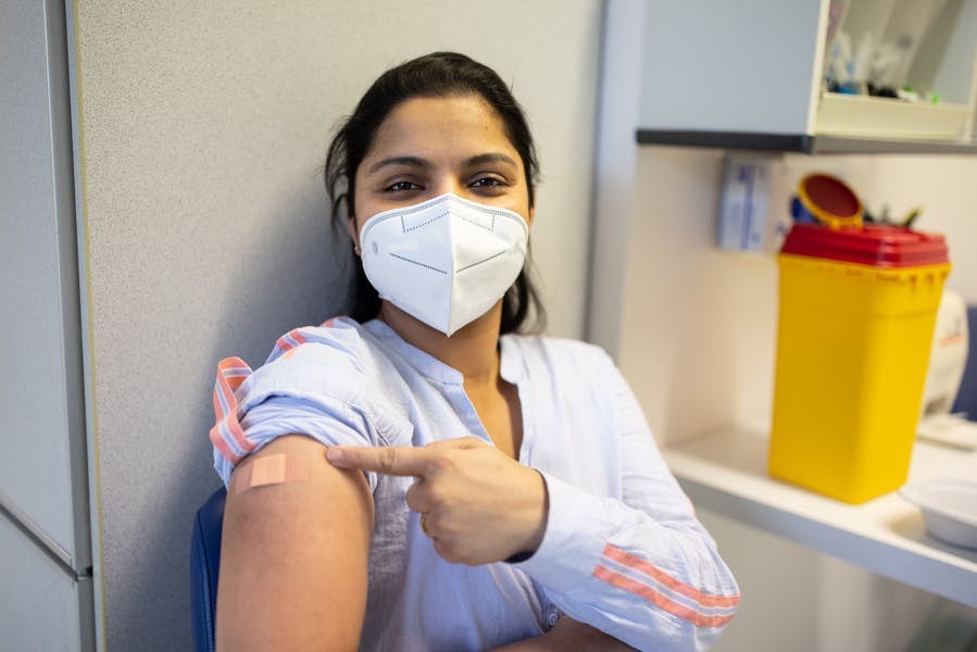 A young, masked woman with a rolled-up sleeve showing her Covid vaccine