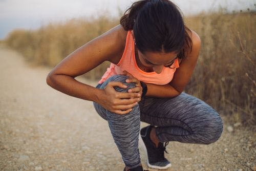 Young woman bent over from knee pain in the middle of jogging on a trail