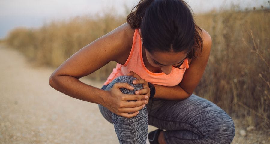 Young woman bent over from knee pain in the middle of jogging on a trail