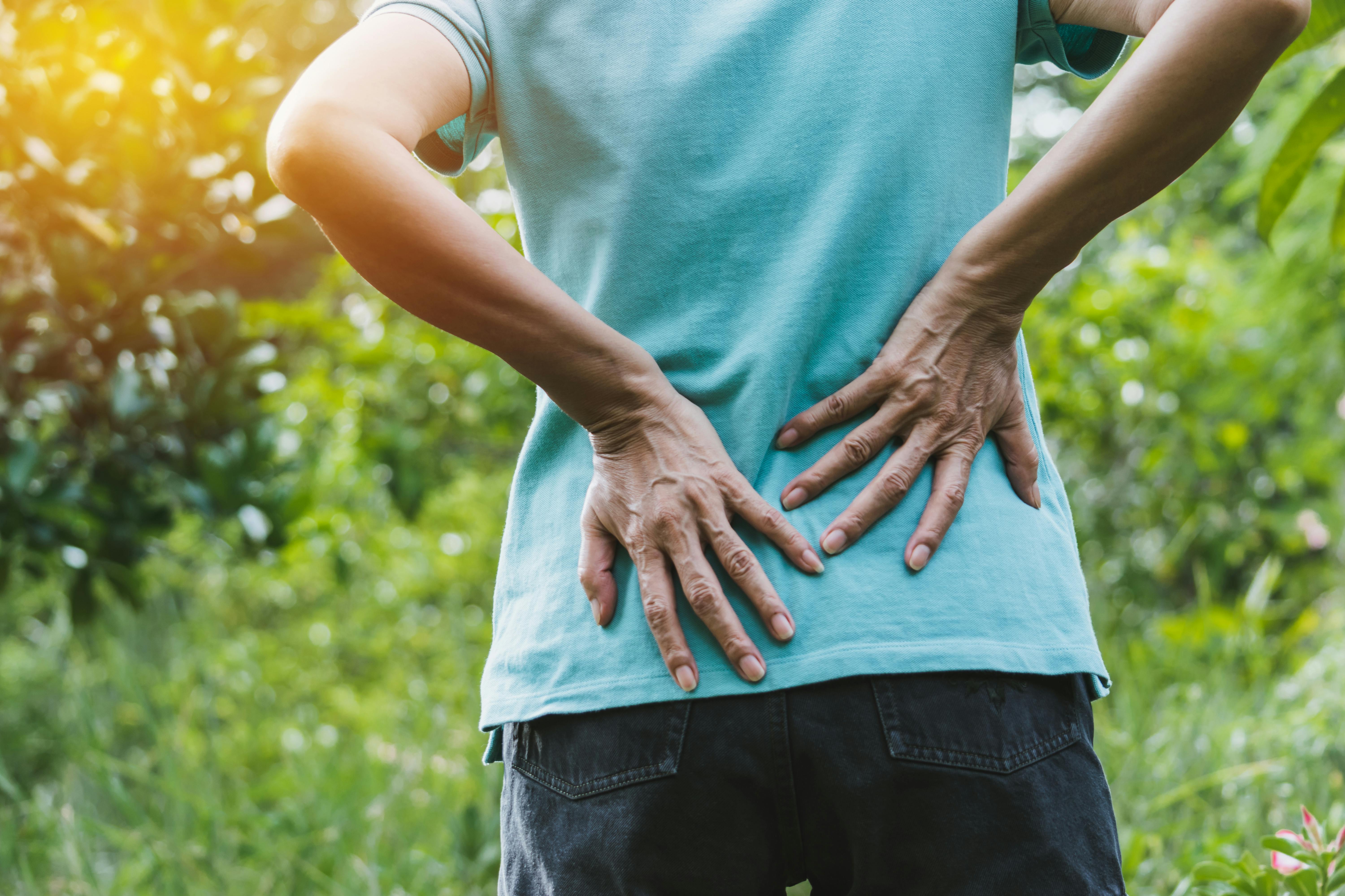 Close-up of a woman’s hands on her lower back as she stands in nature