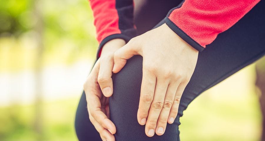 Woman in exercises clothes holding her knee in pain.