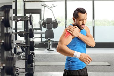 Man at the gym holds sore shoulder