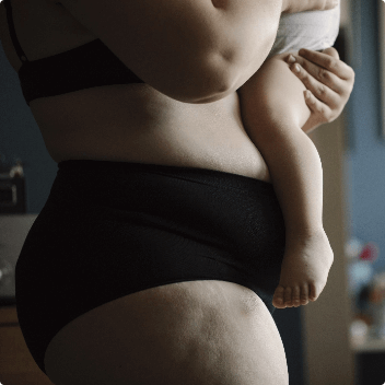 Newly postpartum mother in underwear holding her baby