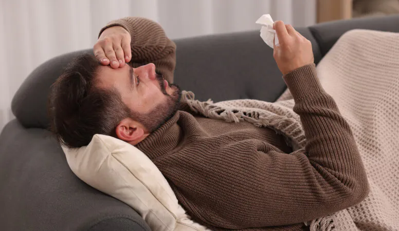 Homme couché sur un canapé et se tenant la tête, en proie à une douleur